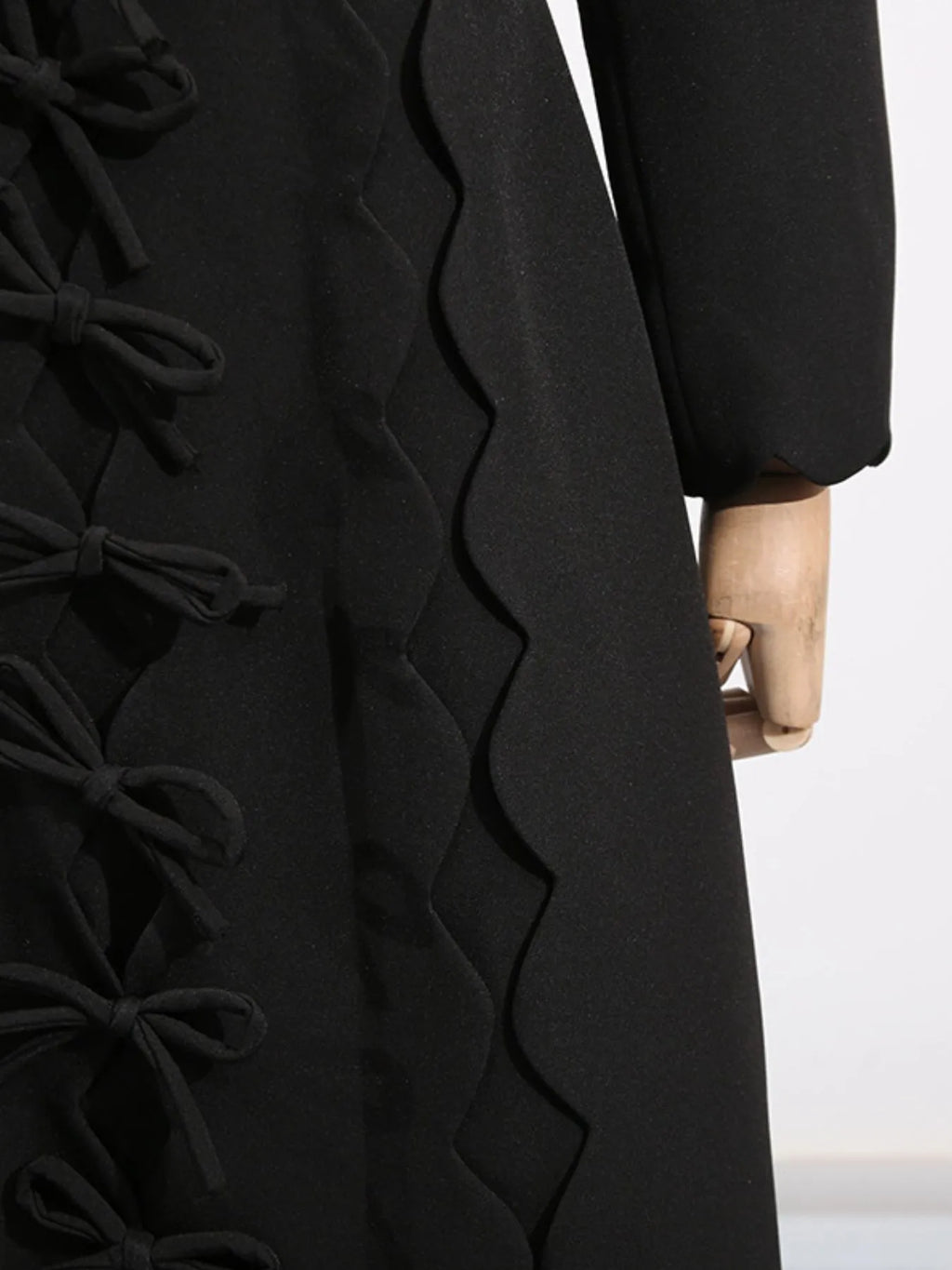 Black long sleeve bow front midi dress with side bow ties scalloped edge and cuffed long sleeve on mannequin