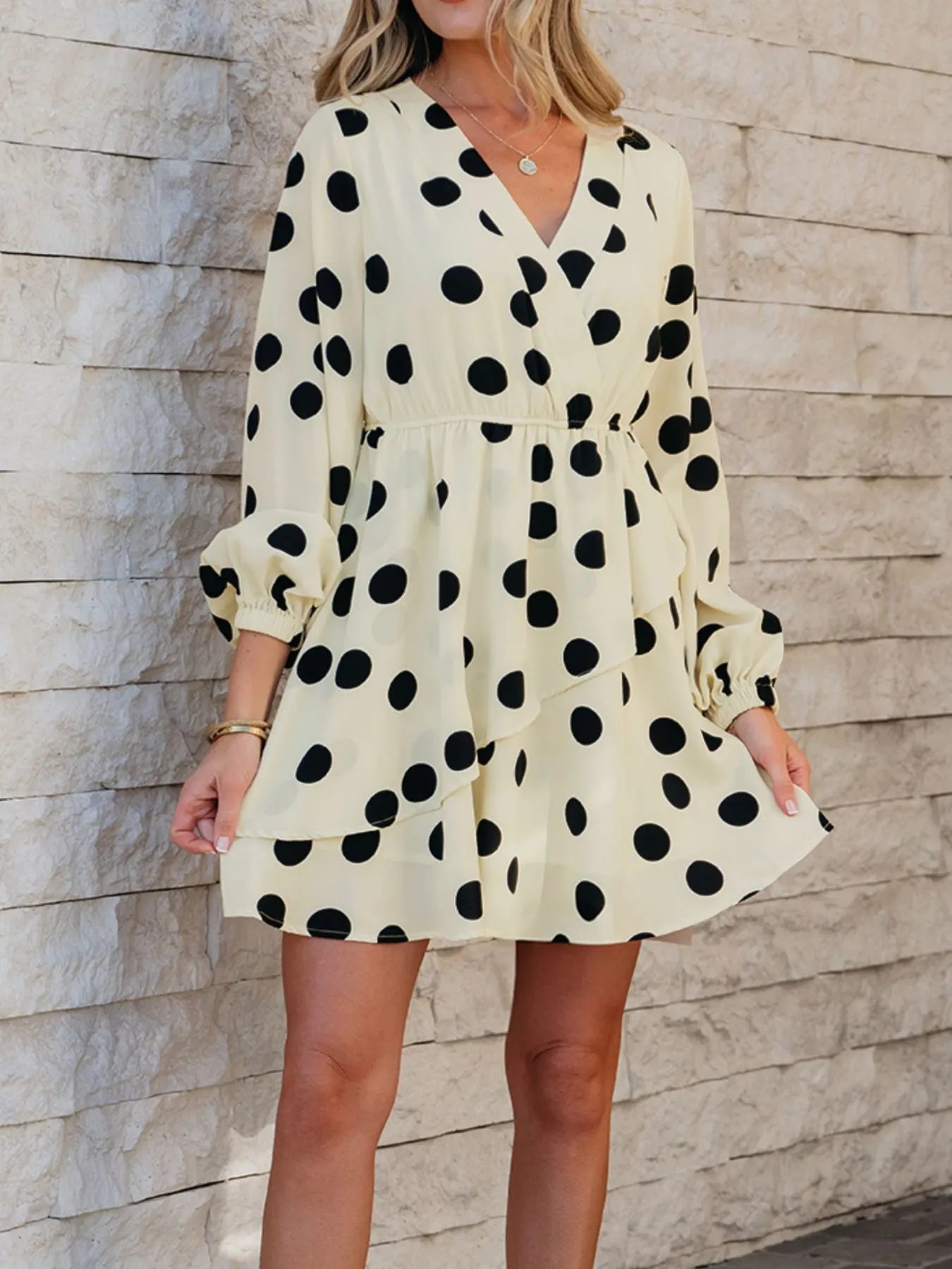 cream polka dot mini dress with V neck long sleeves and tiered ruffle skirt on model