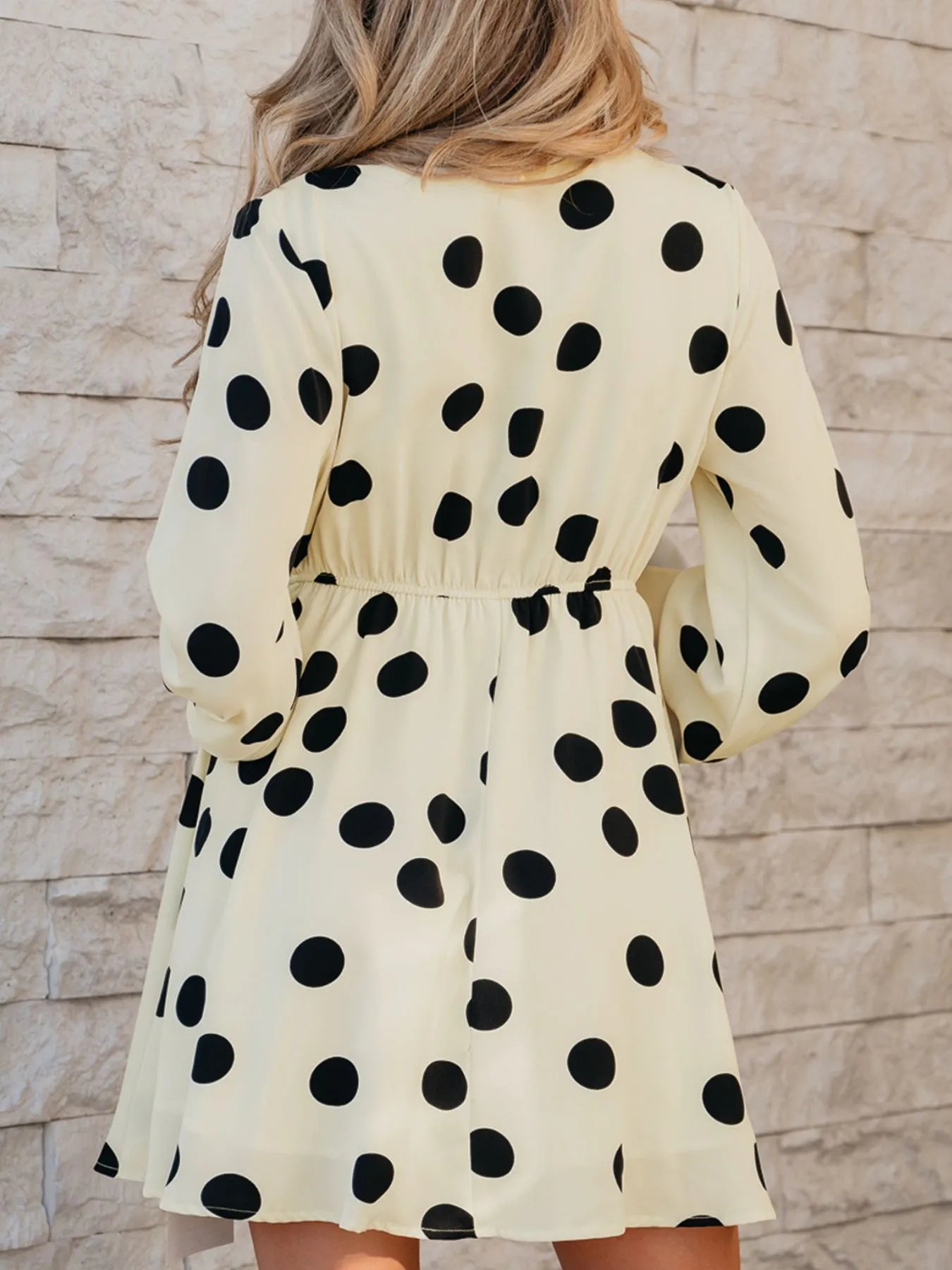 Back view of woman wearing Trendsi polka dot mini dress in cream with black dots elastic waist long sleeves