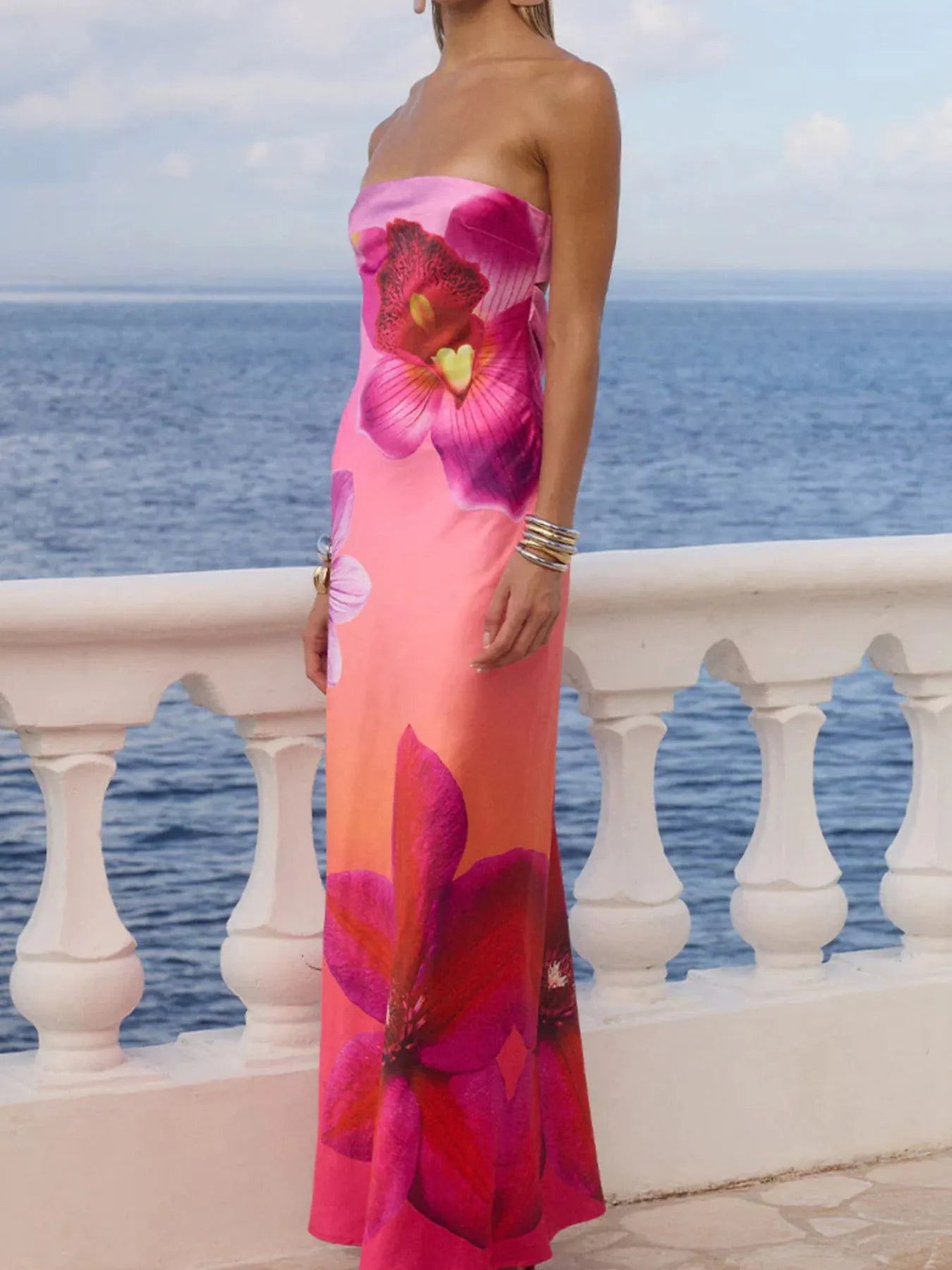 printed tube maxi dress in pink floral gradient worn by model on seaside terrace with gold bracelets