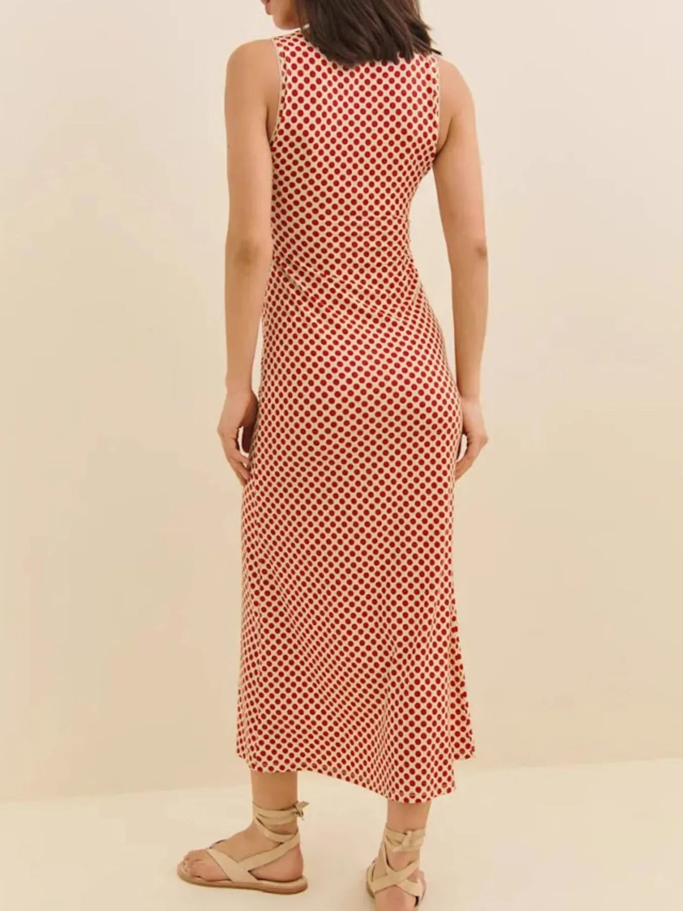 Back view of model wearing red polka dot midi dress sleeveless fitted silhouette with sandals