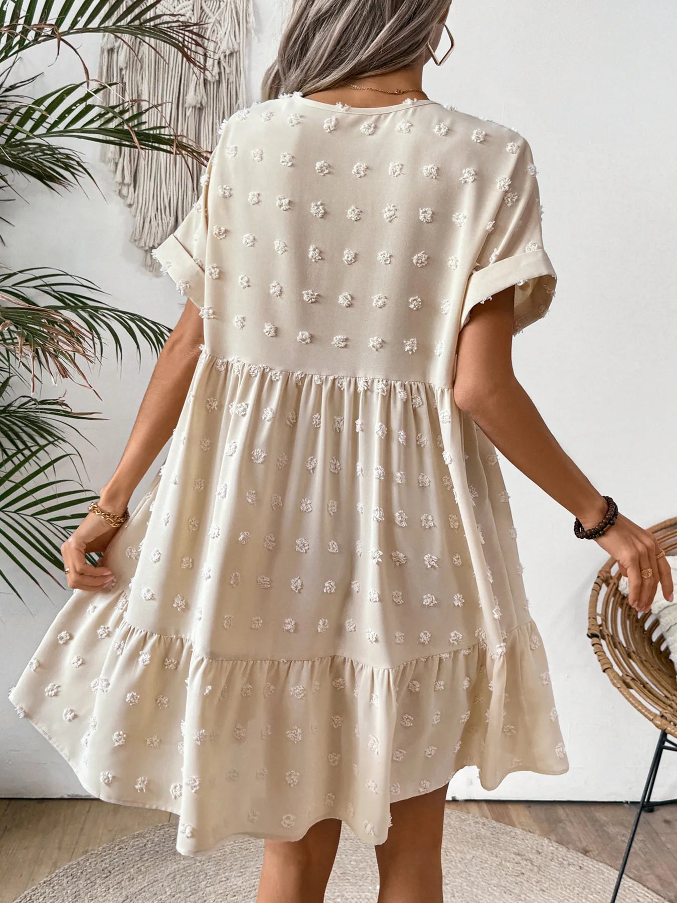 Back view of woman in cream ruffled hem swiss dot mini dress with short sleeves and tiered babydoll silhouette