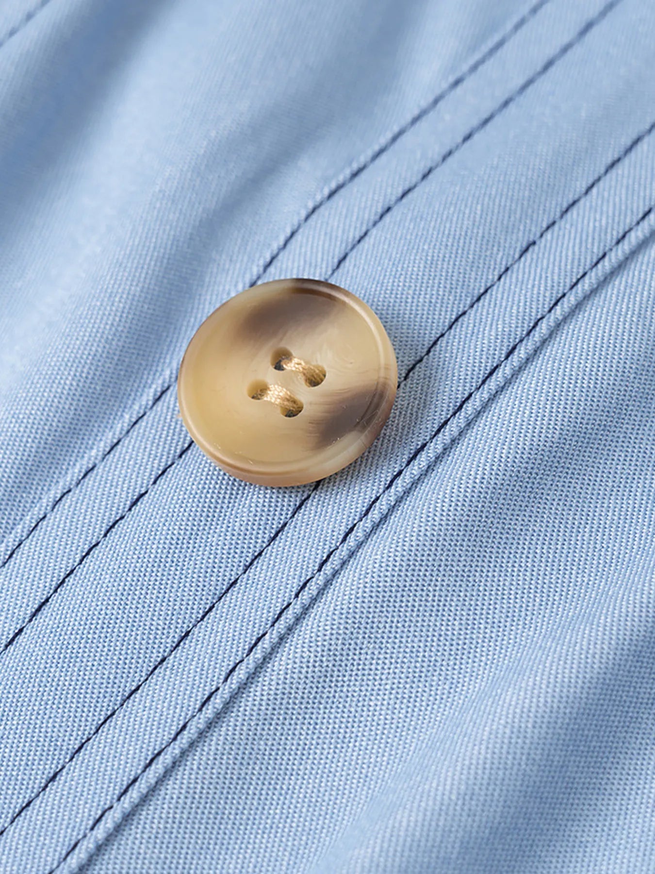 light blue wide strap denim dress close up of tan button and stitched seams on denim fabric