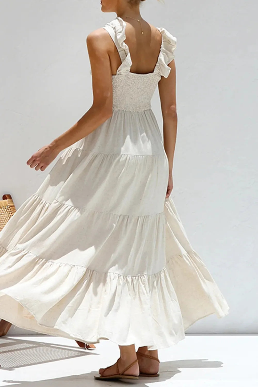 Woman wearing a cream ruffled v-neck tiered dress with smocked bodice ruffled straps and flowing tiers