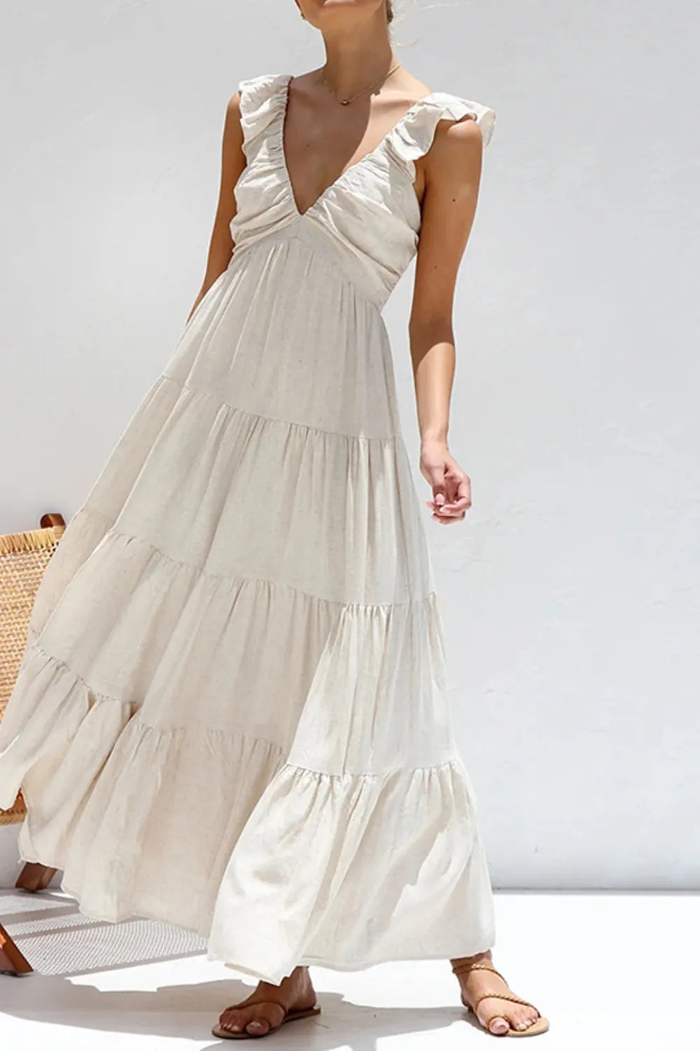 model wearing a cream ruffled v-neck tiered dress with flutter straps and flowing maxi skirt