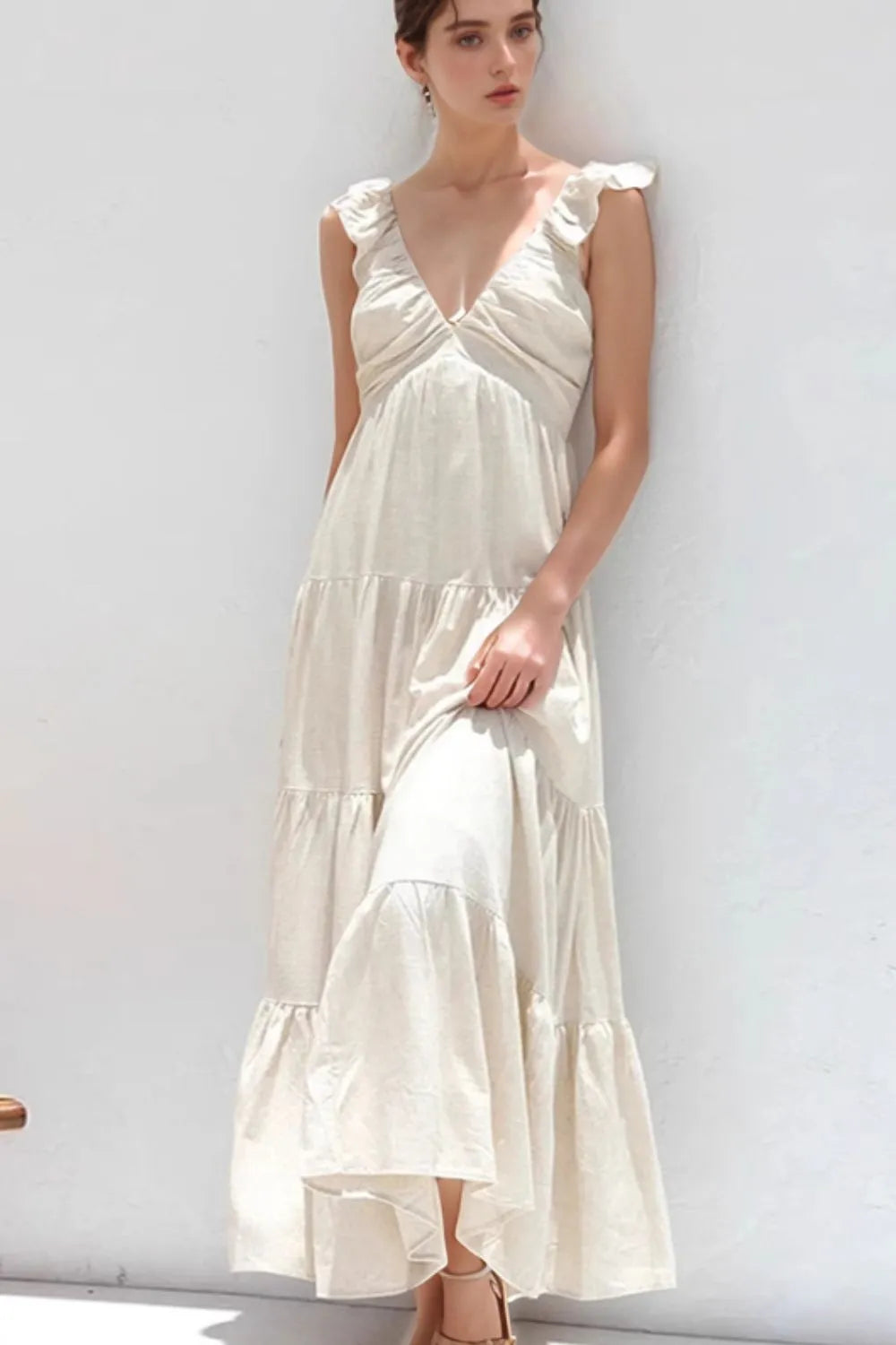 model wearing cream ruffled v-neck tiered dress with flutter straps and flowing maxi silhouette