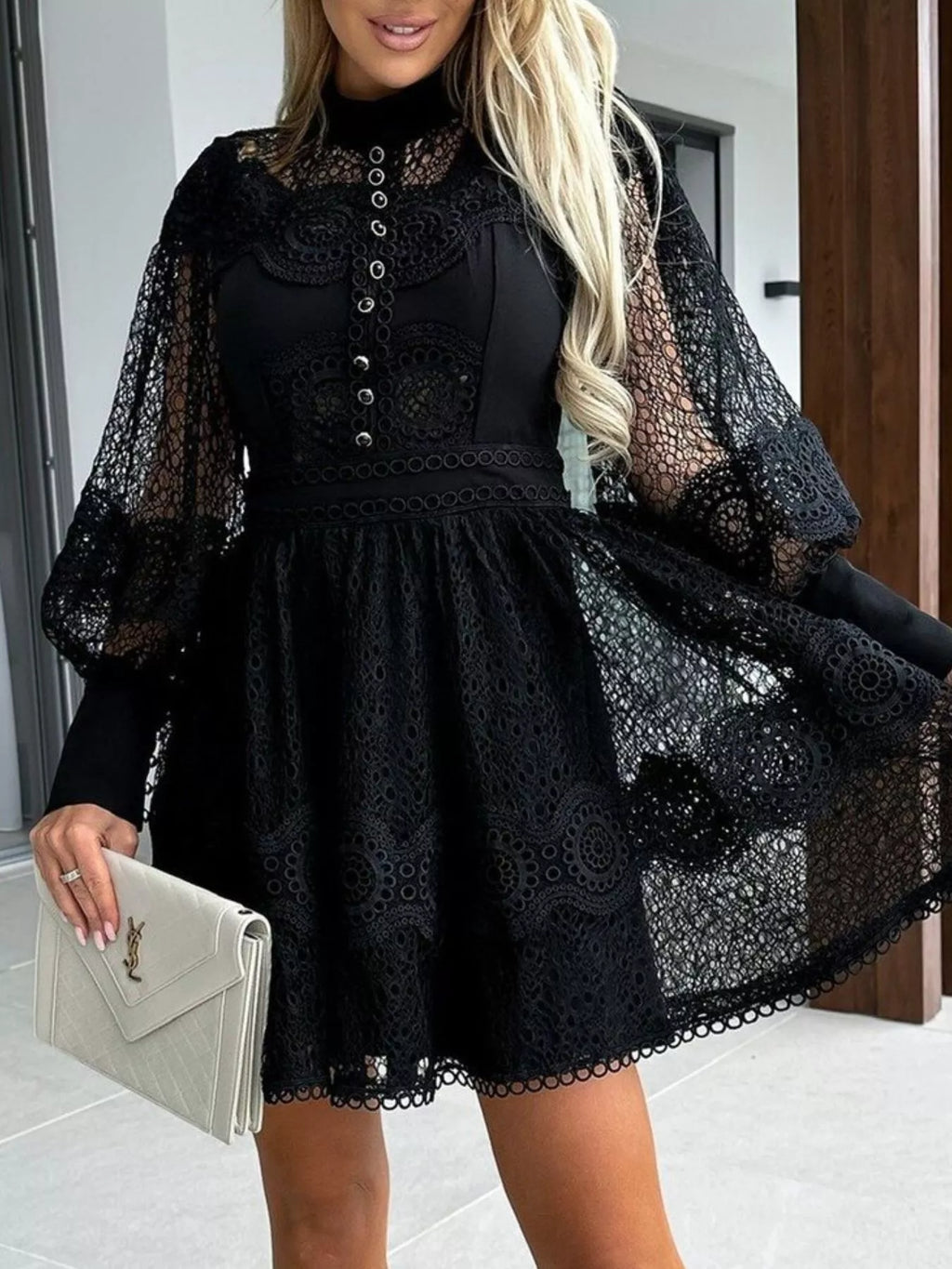 Woman wearing black lace lantern sleeve mini dress with high neckline button front puff sleeves and beige clutch