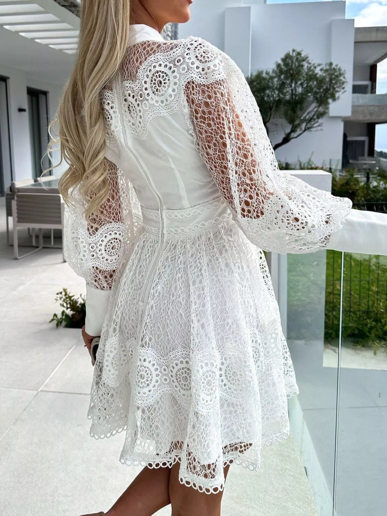 Back view of model in white lace lantern sleeve mini dress with crochet panels fitted waist and flared skirt