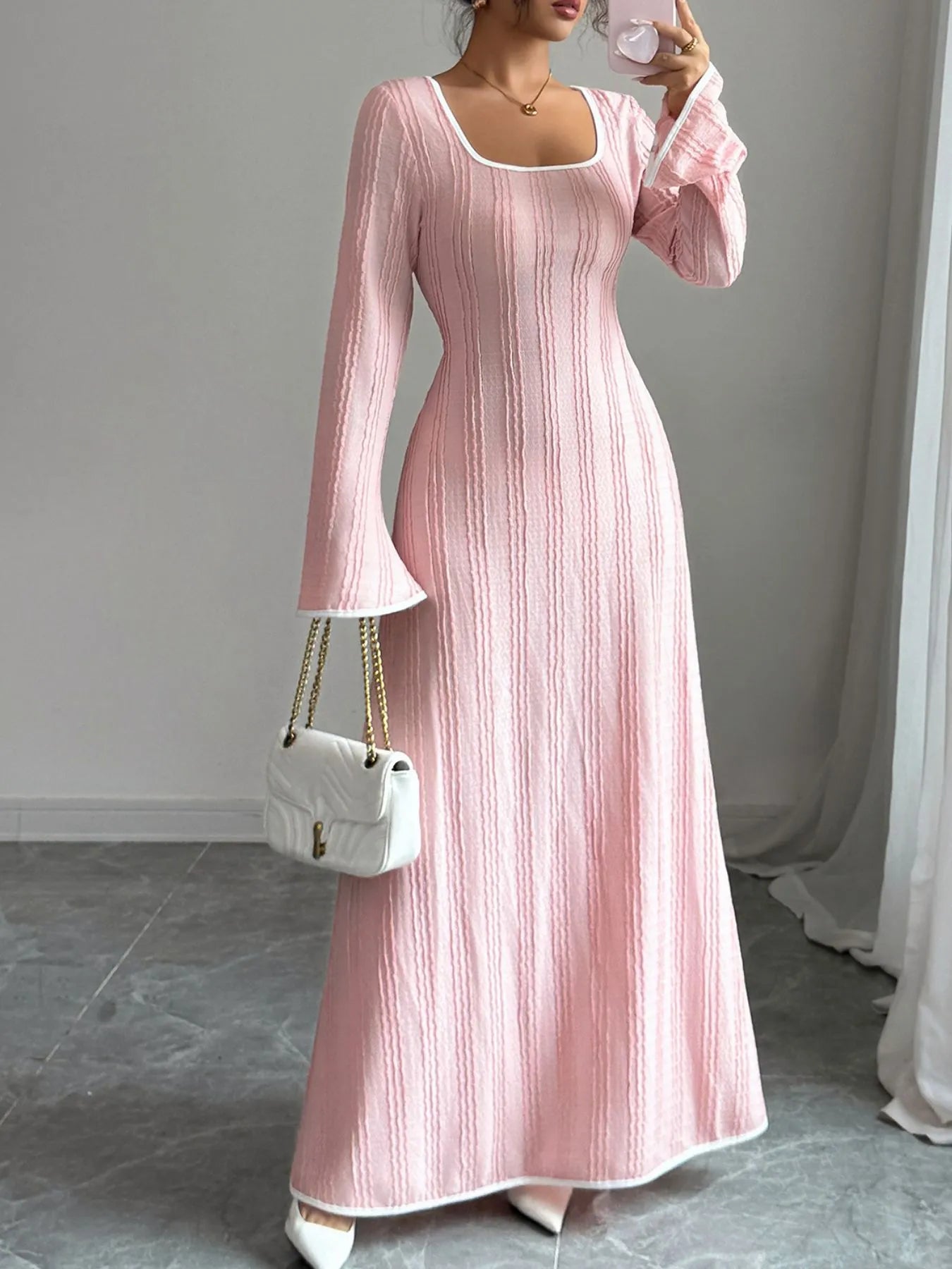 Model wearing a pink textured square neck maxi dress with long bell sleeves fitted waist and white handbag
