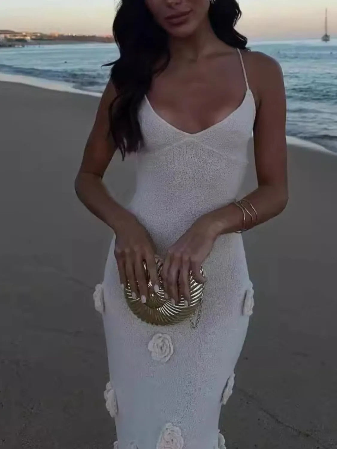 white flower maxi sweater cami dress with spaghetti straps and floral appliques holding gold clutch on beach