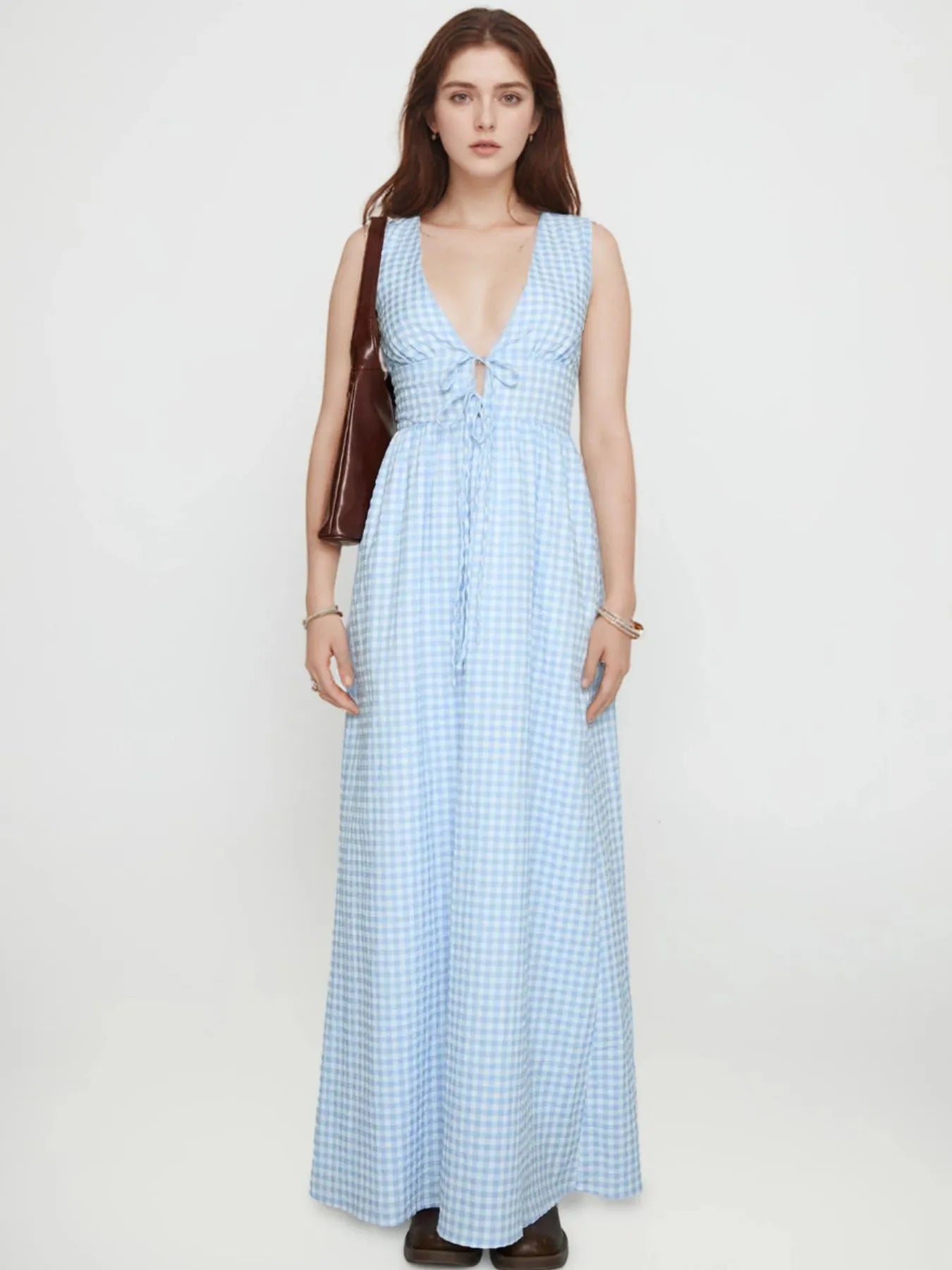 Model wearing light blue plaid tie front maxi dress with deep V neckline sleeveless and brown shoulder bag