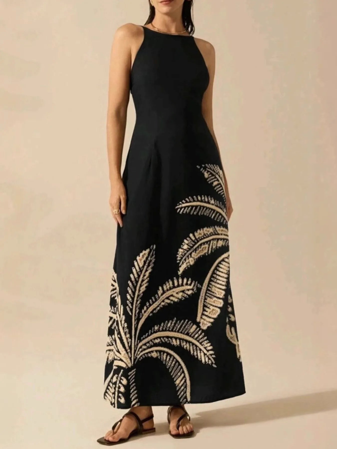 Black halter neck printed sleeveless maxi dress with cream palm print hem fitted bodice and A line skirt on model wearing sandals
