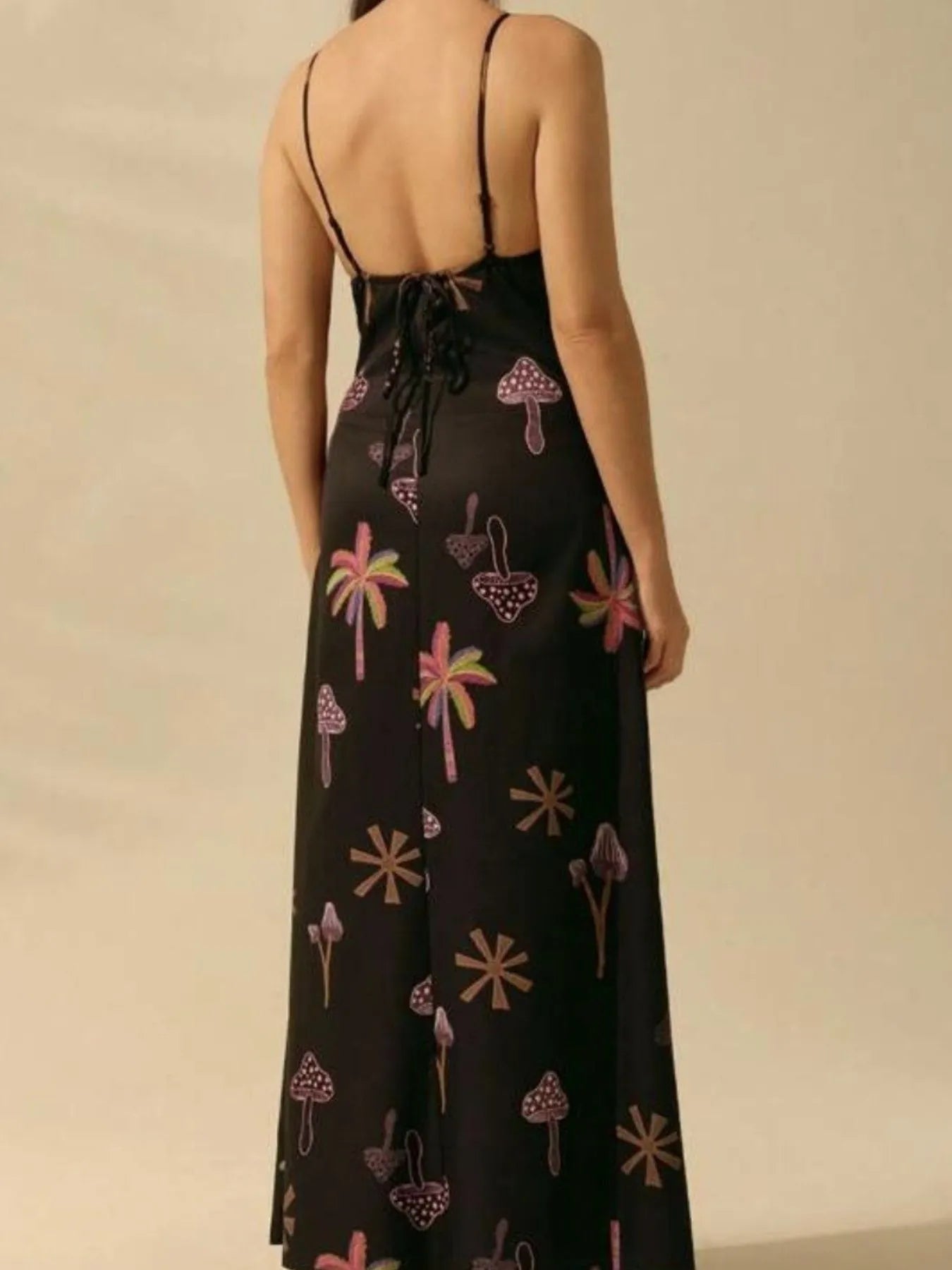 Back view of woman in a black printed sleeveless maxi dress with spaghetti straps lace up back and colorful mushroom palm print