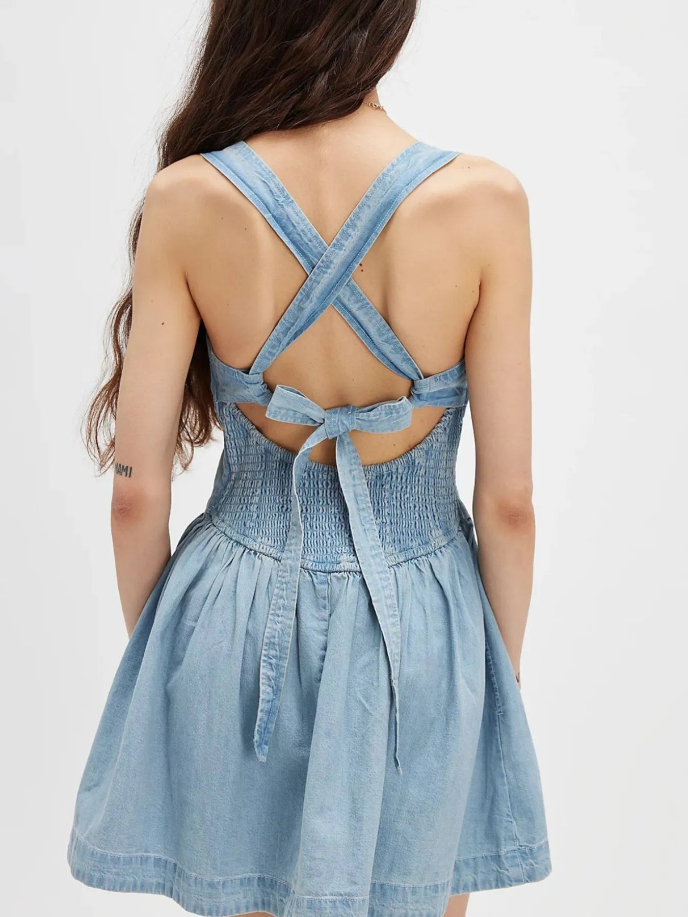 smocked denim mini dress back view with crossed straps, tie back bow and gathered skirt in light wash