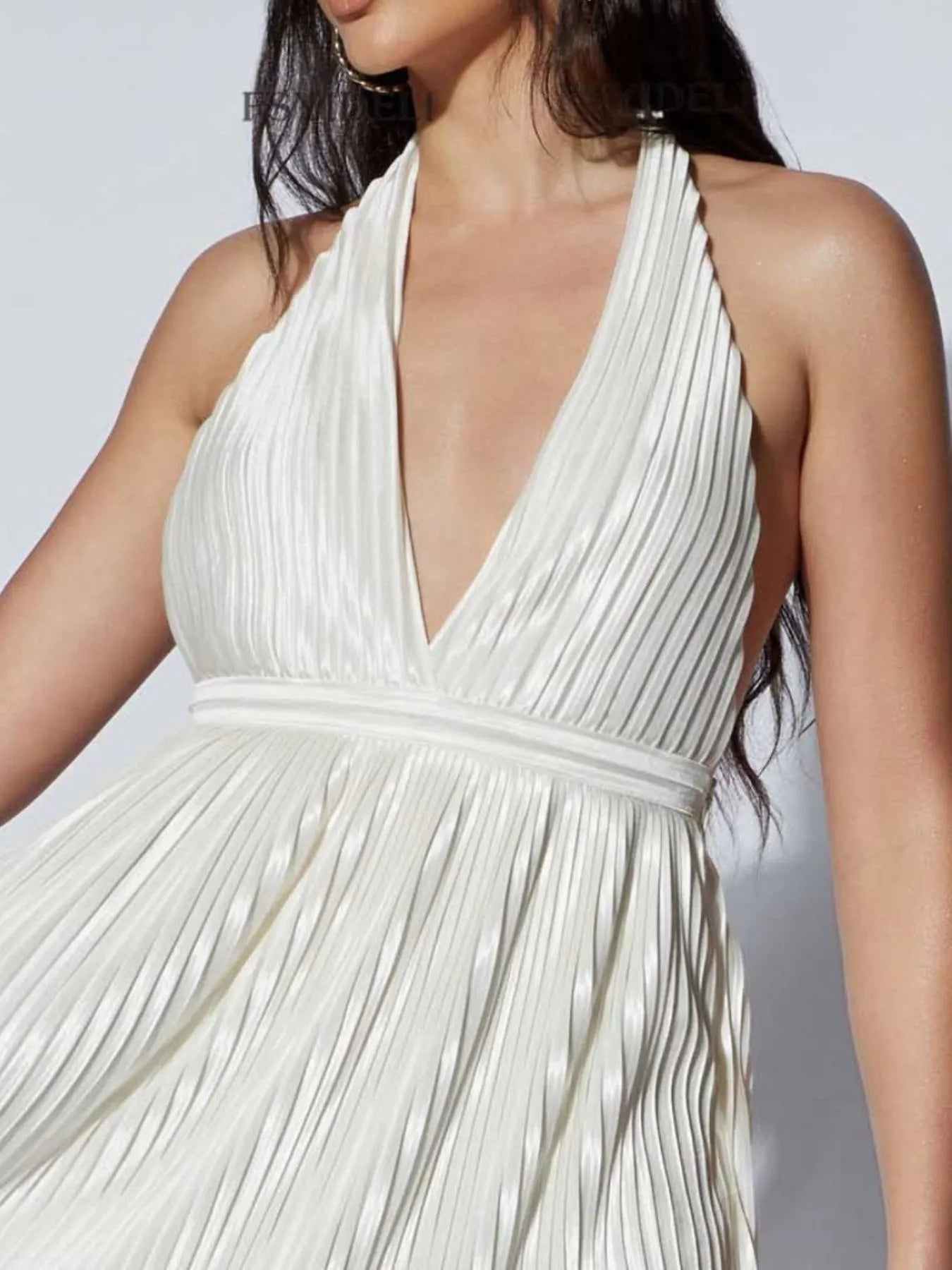 white pleated halter neck mini dress with deep V neckline and cinched waist on model