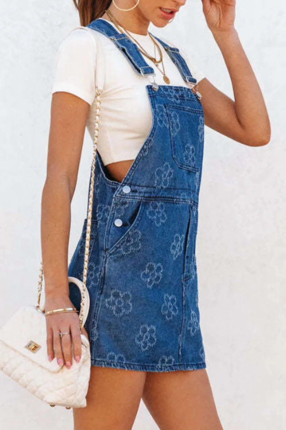 flower print denim overall dress worn over white tee with side pockets and quilted crossbody bag